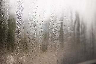 Image of water droplets forming on a window. Someone has touched the water droplets and there are finger streaks going through the water.