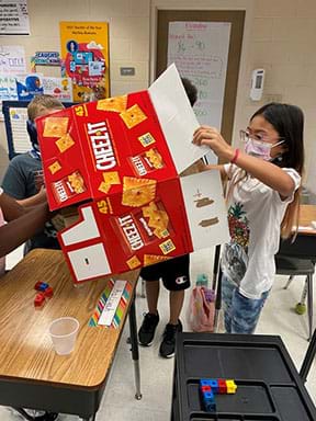 A student observes a cardboard box to plan for how to engineer a personal snack holder.
