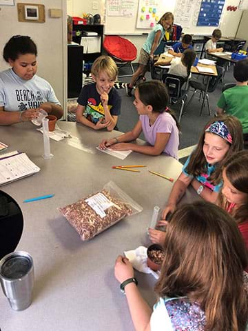 A group of elementary school students works at a table to design drought-resistant soil.