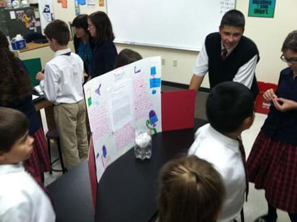 A photograph shows numerous youngsters milling around a classroom table on which sits a student-made water filter and a poster that explains the water filtration process.