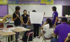 Photo shows four students standing in front of a class, holding a large map and making a presentation.