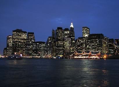 A view of Manhattan at night probably from boat.  Buildings and port structures are brightly lit.