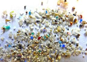 A close-up photograph shows various types, colors and shapes of small plastic particles.