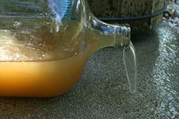 A photograph shows brownish, cloudy dirty water spilling from a clear glass gallon jug lying on its side.