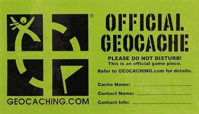 A graphic shows the label for an official geocache artifact. It is a green label with black lettering and the official geocache emblem—a cartoon of a person tracking towards a waypoint flag searching for a hidden treasure. Users are required to submit the cache name, contact name, and info.