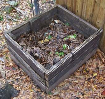 A photograph shows an open box made of boards sitting next to a fence outdoors, and partially filled with food scraps and leaves.