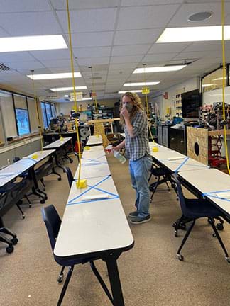 A teacher wiping down desks in a classroom during the COVID-19 pandemic.