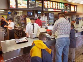 A photograph shows the inside of a fast food restaurant, with a man and two boys at the counter and employees working behind the counter.