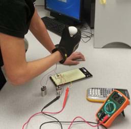 A photograph shows a gloved hand—a student-designed tactile feedback system "robotic hand"—applying pressure to an egg." The glove is wired to a nearby breadboard and multimeter.