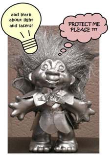 Photo shows a bronzed troll doll with bubble captions: "Protect me, please???" and "and learn about light and lasers!"