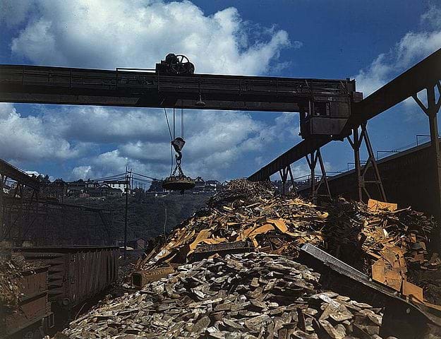 A photograph shows carloads of scrap metal being sorted and moved at the Allegheny Ludlum Steel Corp. in Pennsylvania in the 1940s. An overhead magnet deposits the scrap in a loader that carries it to a furnace to be melted down for re-use.