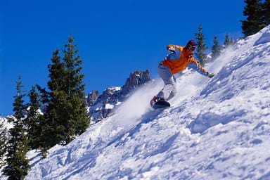 Photo shows a man snowboarding down a steep slope.
