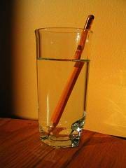 Photo shows a side view of a pencil in a glass of water. The pencil image is refracted at the point where the pencil enters the water.