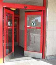 Photo shows double glass doors partially opening inward at store entrance with a sensor positioned above the doorway.