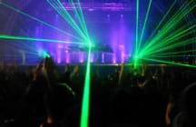Photo shows beams of green light directed at a darken audience as part of a laser light show from a concert stage.