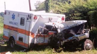 Photo shows an ambulance damaged from a crash. The front cab of the truck is crumpled and torn away from a dented back section.