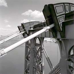 Photo shows close-up of cables at top of a bridge tower.