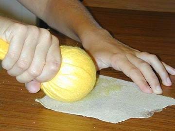 A photograph shows a hand holdin the ends of fabric that is wrapped around a fist-sized ball, while pulling across a piece of sand paper.