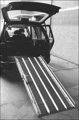 A black and white photo shows a ramp with side edges leaning from the open back of a vehicle to the ground.