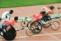 Photo shows a wheelchair race with four competitors in blurred motion.