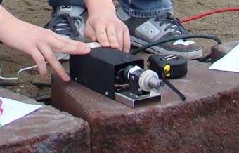 Photo shows a small black box device on a stone block.