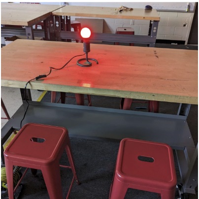 A photo showing a lamp without a cover with a red bulb turned on at the center of a desk. 