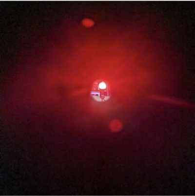 An image through a circular black tube lens of a lit red light bulb, which is clear and slightly magnified.