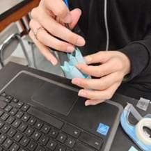 A photo showing a student using a pencil to secure the light and heavy chains of the antibodies. The flaps on the heavy chain have double-sided tape to adhere the two parts of the antibody together.