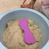 A photo showing a pink foam orthotic insole lying on top of a bin filled with modeling sand. A student’s hand rests beside the container. A photo showing a pink foam orthotic insole lying on top of a bin filled with modeling sand. A student’s hand rests beside the container.