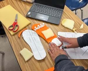 A photo of a student using their hands to form a moldable foam on top of an orange orthotic shoe insole. A photo of a student using their hands to form a moldable foam on top of an orange orthotic shoe insole.