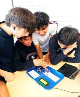 A photo showing four students working collaboratively to program an Arduino air quality monitor.