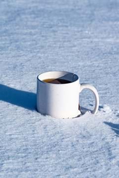 A photo showing a mug of dark liquid sitting on top of snow. A photo showing a mug of dark liquid sitting on top of snow.