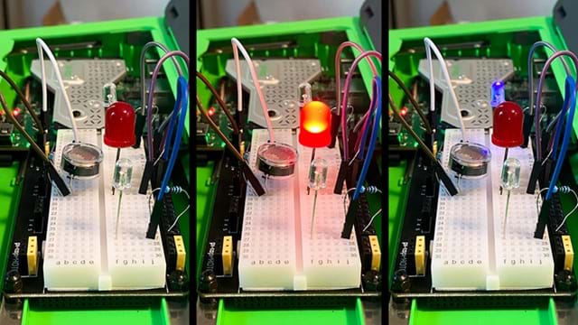 A photo showing a small electronics breadboard setup inside a green plastic case. The breadboard has several components inserted: three LEDs, a small circular sensor, resistors, and multiple jumper wires connecting the components to the underlying circuit board. A photo showing a small electronics breadboard setup inside a green plastic case. The breadboard has several components inserted: three LEDs, a small circular sensor, resistors, and multiple jumper wires connecting the components to the underlying circuit board.