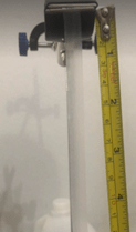 An image showing a stress testing setup. A strip of material is clamped at the top of a lab stand. The strip is vertically suspended, and measuring tape is aligned next to the strip measuring the length of the strip. 