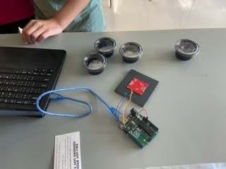 A photo showing students working at their lab station to complete the setup, including a laptop device, four sample cups, and a spectrometer connected to device.