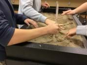 A photo showing students using their hands to create a river channel with a width of two fingers.