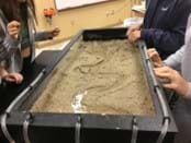 A photo showing students around a stream table with water flowing through.