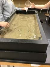 A photo showing students around a stream table with water flowing through.