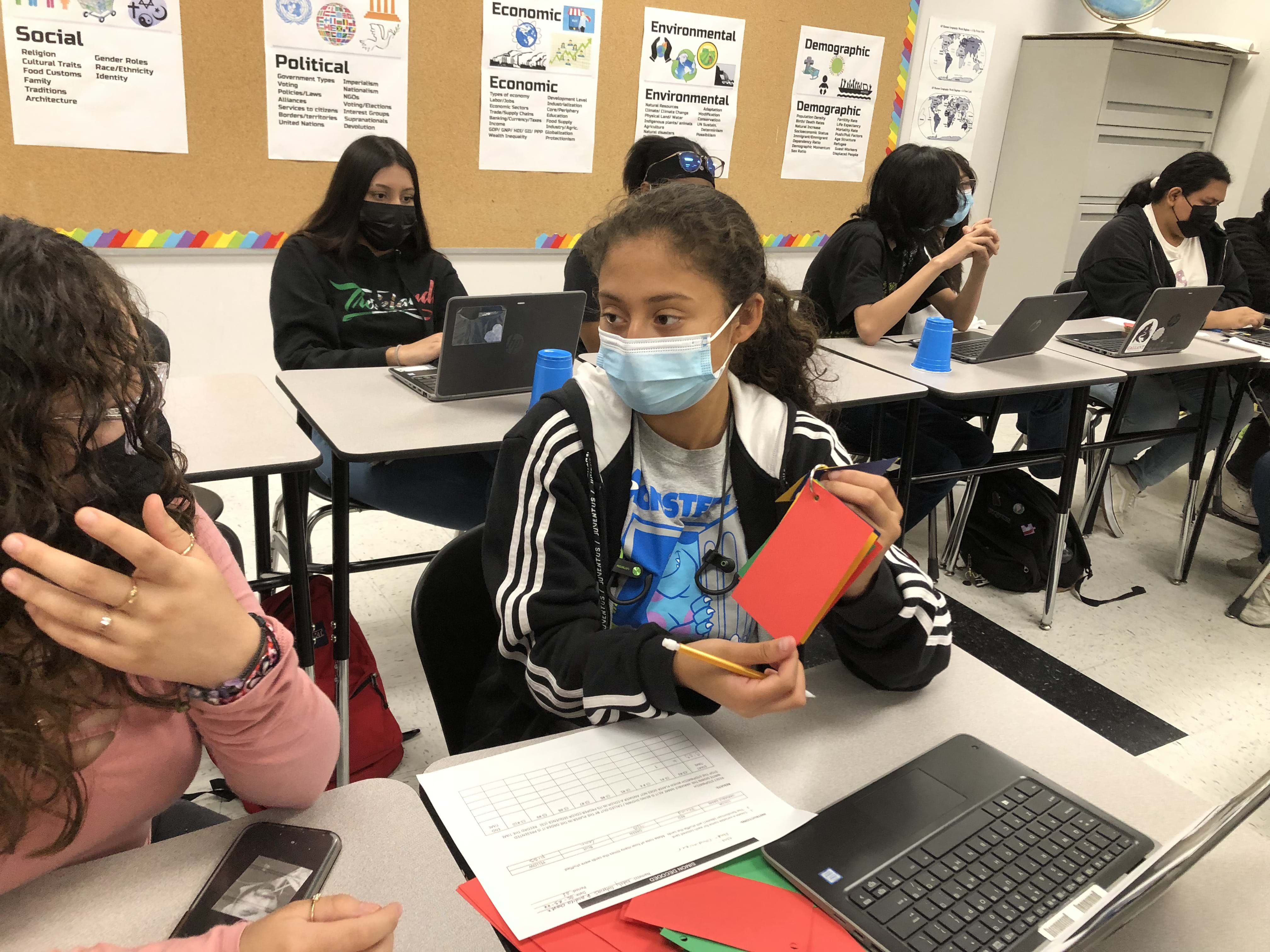 A photo of a student holding up a red index card to show another student. 