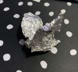 A photo of aluminum foil that has been pressed into a shape that has wings for a student’s creature against a black and white polka-dot background.