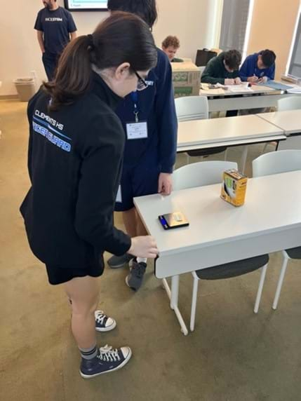 A photo of students measuring the mass of the fabric they cut on a small digital scale.