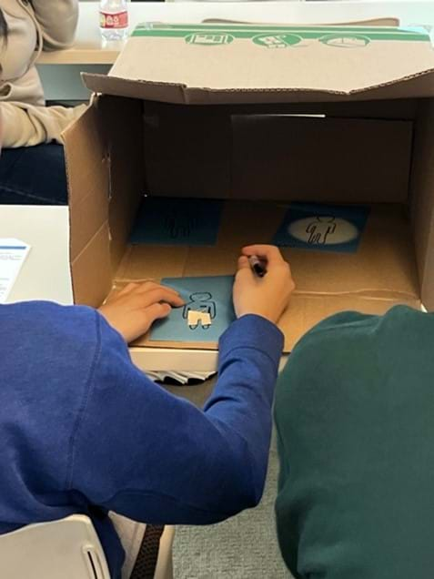 A photo of a student working inside the box to adjust their cut cotton fabric to fit the person-shape on their photoluminescent paper.