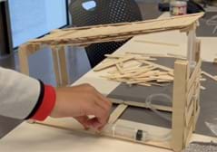 A photo showing a bridge constructed from popsicle sticks, with a rectangular platform as the base and a rectangular platform as the top/bridge portion. The top platform is held up in each corner using 2 wide popsicle sticks glued vertically to form a corner. The front of the bridge has a wall between 2 corners that is holding one syringe and the plastic tubing. The second syringe is attached to the base using zip ties. When the syringe on the base is pressed, it causes the syringe attached to the front wall to push up vertically and raise the top platform. The platform is lowered by pulling the syringe attached to the bottom base. A photo showing a bridge constructed from popsicle sticks, with a rectangular platform as the base and a rectangular platform as the top/bridge portion. The top platform is held up in each corner using 2 wide popsicle sticks glued vertically to form a corner. The front of the bridge has a wall between 2 corners that is holding one syringe and the plastic tubing. The second syringe is attached to the base using zip ties. When the syringe on the base is pressed, it causes the syringe attached to the front wall to push up vertically and raise the top platform. The platform is lowered by pulling the syringe attached to the bottom base.