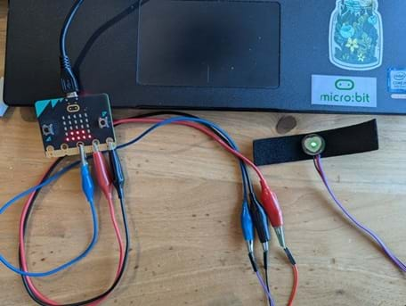 A photo showing a micro:bit connected to the pulse sensor using alligator clamps. From the pulse sensor to the micro:bit, black is connected to GND, red is connected to 2V, and purple is connected to Pin #2.