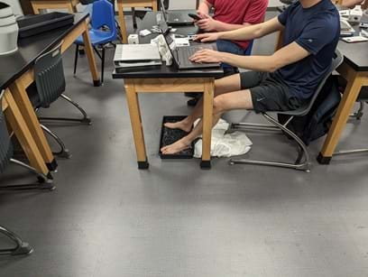 A photo of a student coding at his computer, “getting into the zone,” while his feet are in an ice water footbath.