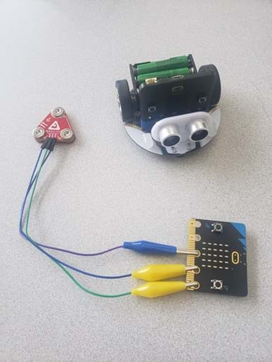 A photo showing an assembled Cutebot robot sitting on a gray surface next to a MyoWare muscle sensor attached to a micro:bit with wires.