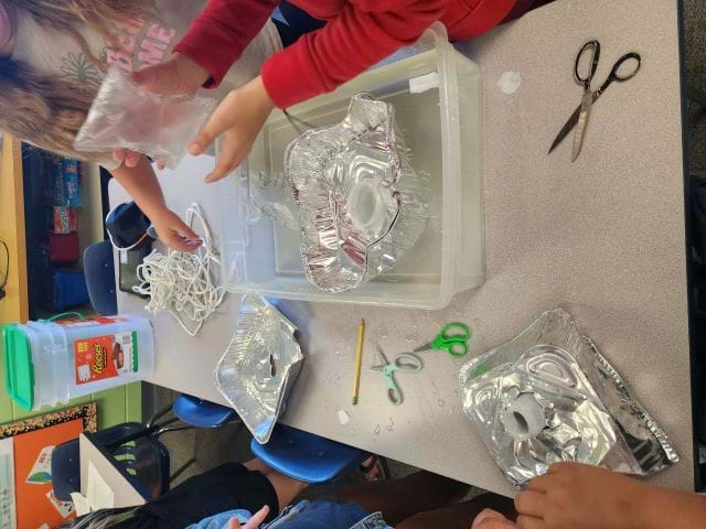 A photo showing students using recycled materials such as aluminum foil to build aquaponic pots to grow lettuce.