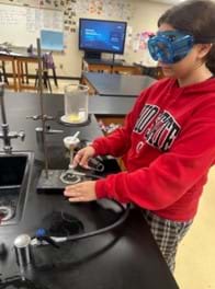 A photo of a student standing in front of a Bunsen burner and ring stand. A beaker with a yellow leaf in it is on top of the wire mesh on top of the ring clamp clamped to the ring stand. A photo of a student standing in front of a Bunsen burner and ring stand. A beaker with a yellow leaf in it is on top of the wire mesh on top of the ring clamp clamped to the ring stand.
