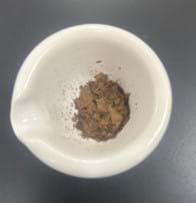 A photo of a mortar with a crushed-up, brown, dried leaf-like substance in it. A photo of a mortar with a crushed-up, brown, dried leaf-like substance in it.