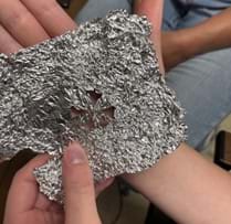 A photo showing a student holding aluminum foil with a pattern cut into it. A photo showing a student holding aluminum foil with a pattern cut into it.